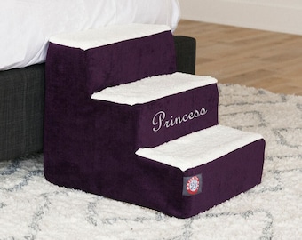May include: Purple pet steps with a white sherpa top and the word "Princess" embroidered on the second step. The steps are on a white shag rug.