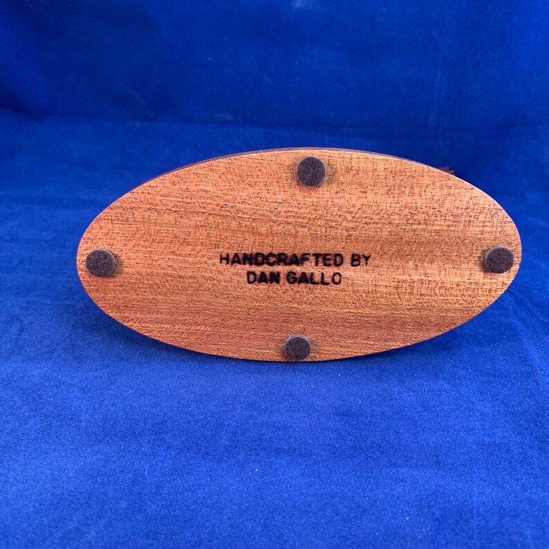 May include: A wooden oval base with four black felt pads on the bottom. The base is engraved with the text "HANDCRAFTED BY DAN GALLO".