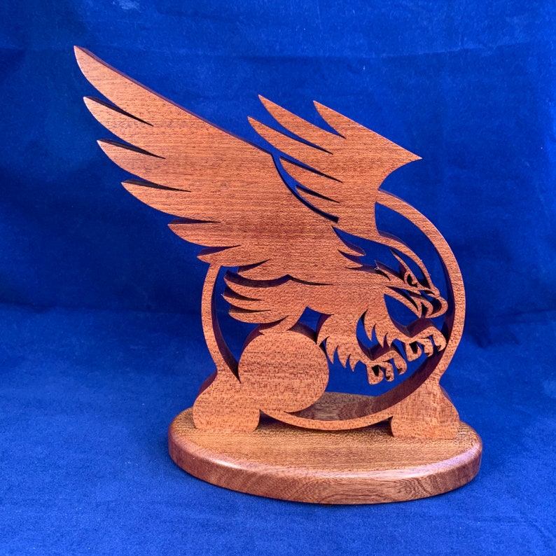 May include: A wooden sculpture of an eagle with its wings spread, holding a sphere in its talons. The sculpture is mounted on a wooden base.