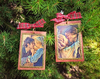 May include: Two rectangular Christmas ornaments with romantic artwork, each adorned with a red plaid bow. The artwork depicts a couple kissing. The ornaments are hanging on a green Christmas tree.