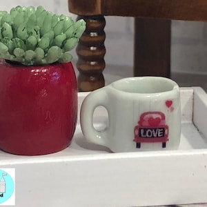 May include: A white tray with a red potted succulent and a white mug with a pink car and the word "LOVE" on it.