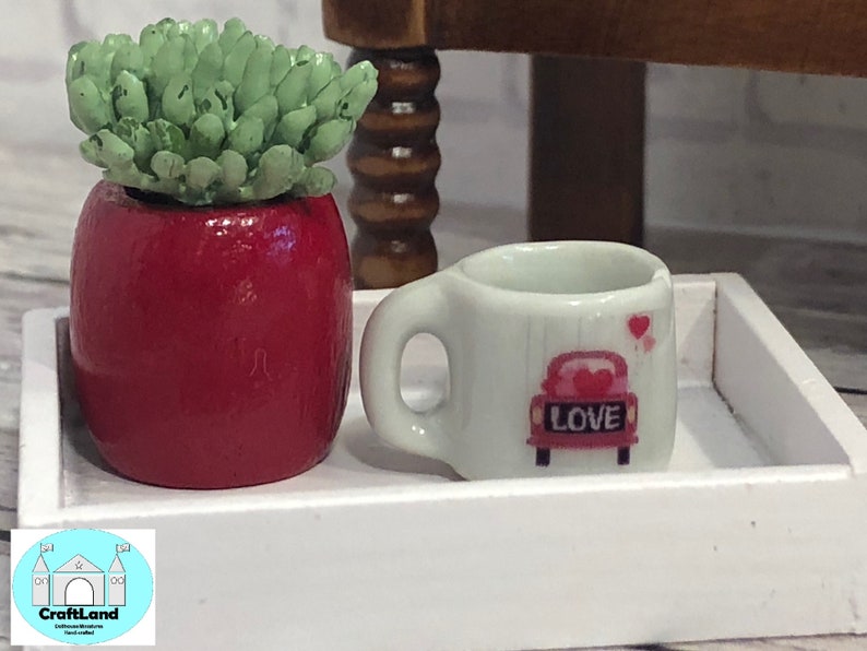 May include: A white tray with a red potted succulent and a white mug with a pink car and the word "LOVE" on it.
