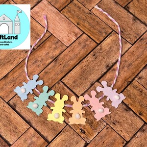 May include: A pastel colored bunny garland with a white string. The garland is made of paper and has a white pom-pom on each bunny.