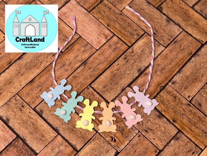 May include: A pastel colored bunny garland with a white string. The garland is made of paper and has a white pom-pom on each bunny.