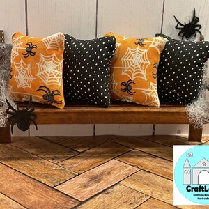 May include: Four miniature pillows with a Halloween theme. Two pillows feature a black and white polka dot pattern, and two pillows feature an orange background with white spiderwebs and black spiders. The pillows are arranged on a wooden bench with a spiderweb design. The bench is on a wooden floor with a herringbone pattern. The image includes the text "CraftLand Dollhouse Miniatures Handcrafted".