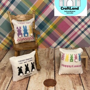 May include: Three miniature pillows with Easter themes. The first pillow is white with black bunny silhouettes and the text "CARROT COMPANY Cake Juice Cookies Locally owned". The second pillow is white with a pink, blue, and yellow bunny silhouette and the text "HOP ON". The third pillow is white with a multi-colored bunny silhouette and the text "Happy Easter".