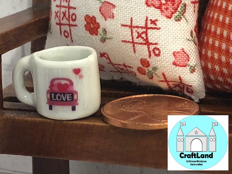 May include: White ceramic miniature coffee mug with a pink car design and the word "LOVE" on the back. The mug is sitting on a wooden surface next to a penny.