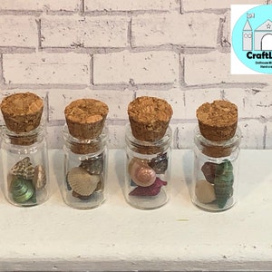 May include: Four small glass jars with cork tops filled with various seashells. The jars are arranged in a row on a white surface. CraftLand Dollhouse Miniatures Hand-crafted.