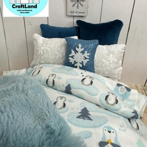 Op de afbeelding: Een poppenbed met een blauwe en witte beddengoedset met pingu&iuml;nmotief. Het bed heeft een blauwe nep bontdeken en verschillende witte en blauwe kussens. Een bord boven het bed staat "Let it snow" met een sneeuwvlokkenontwerp.