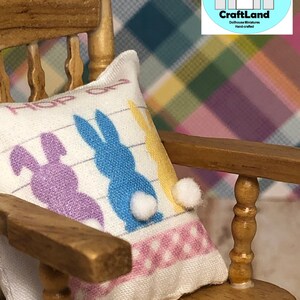 May include: A white pillow with a pink and white polka dot border and three colorful bunny silhouettes. The pillow is sitting on a wooden rocking chair. The pillow has the text "Hop on over" printed on it.