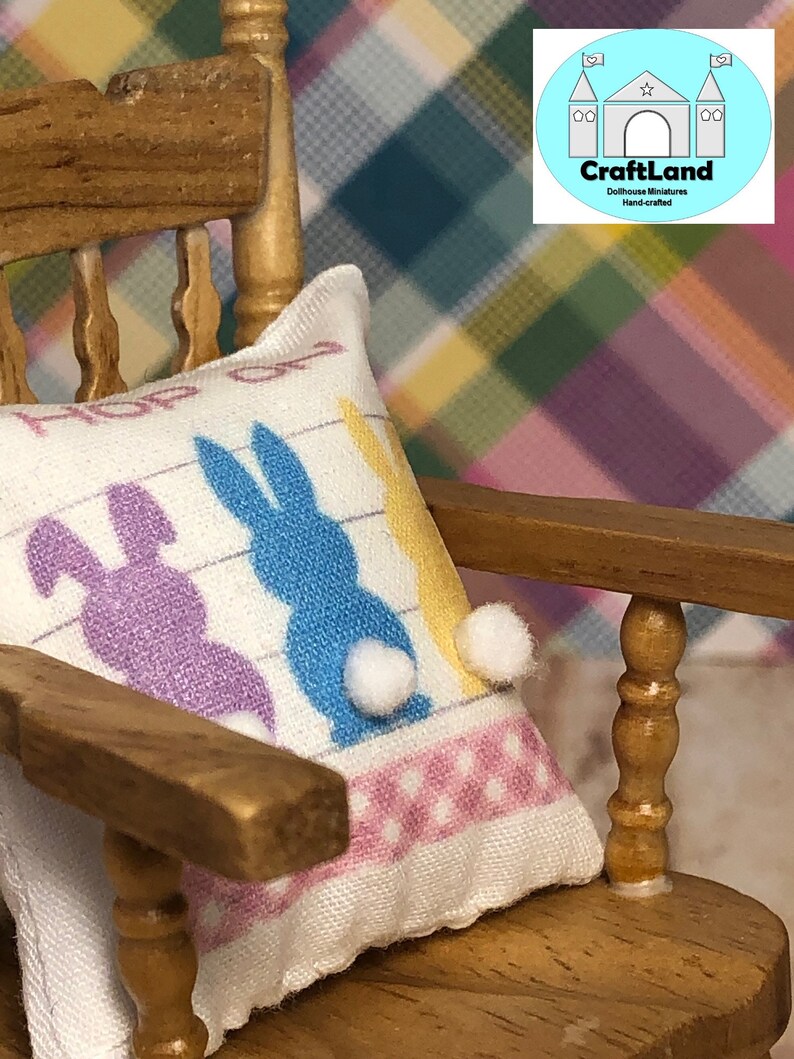 May include: A white pillow with a pink and white polka dot border and three colorful bunny silhouettes. The pillow is sitting on a wooden rocking chair. The pillow has the text "Hop on over" printed on it.