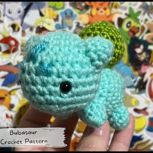 Puede incluir: Un juguete de amigurumi Bulbasaur Pokémon de crochet en azul claro y verde. El juguete está siendo sostenido en una mano. El texto de la imagen dice "Bulbasaur Crochet Pattern".