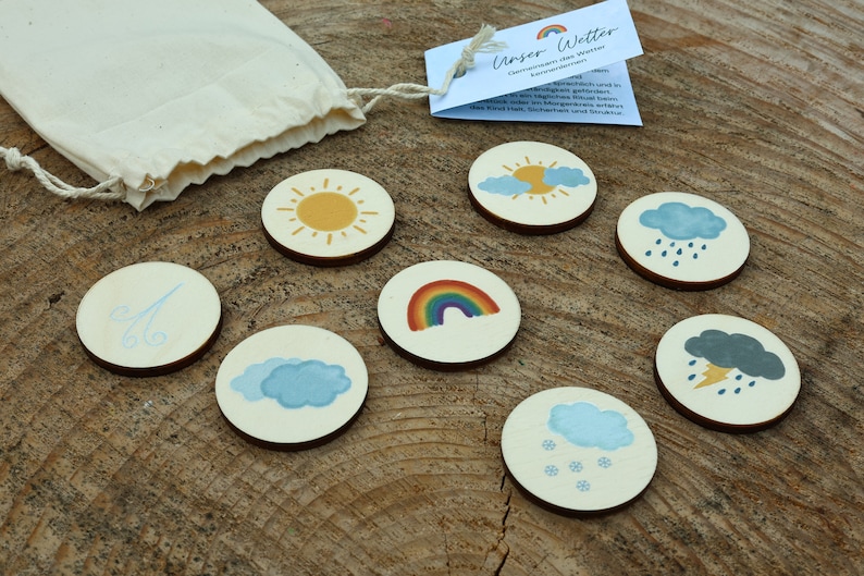 May include: A set of eight wooden weather themed discs with various weather icons, including a sun, clouds, rain, wind, rainbow, snow, and lightning. The discs are in a small white drawstring bag. The text on the card reads "Unser Wetter - Classroom game that weather can be experienced playfully."
