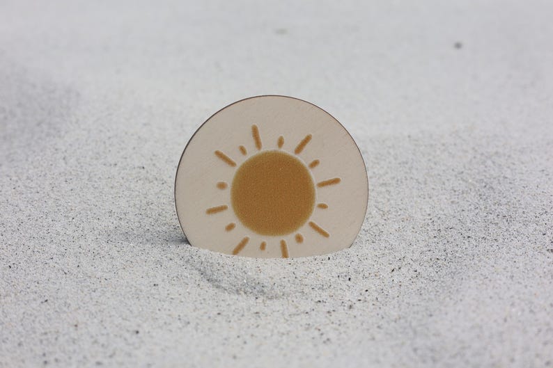 May include: A round, white coaster with a yellow sun design. The sun has a simple, hand-drawn style with rays extending from the center.