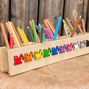 Könnte beinhalten: Holzstiftbehälter mit mehreren Fächern, auf der Vorderseite mit bunten Bagger-Designs. Der Behälter ist mit einer Vielzahl von Buntstiften gefüllt.