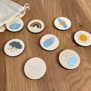 May include: Set of eight wooden weather themed circles with various weather icons including a rainbow, sun, clouds, rain, lightning, snow, and wind.