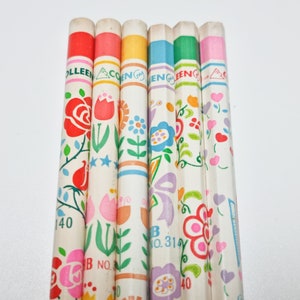 Peut inclure: Un ensemble de sept crayons de couleur avec des motifs floraux. Les crayons sont blancs avec des rayures de différentes couleurs et des motifs floraux. Les crayons sont étiquetés "Colleen" et "B No. 314".