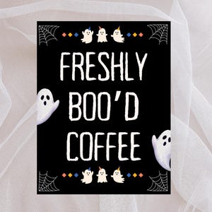 May include: A black sign with white text that reads "FRESHLY BOO'D COFFEE." The sign features cartoon ghosts, spiderwebs, and colorful diamond accents, perfect for Halloween decor.