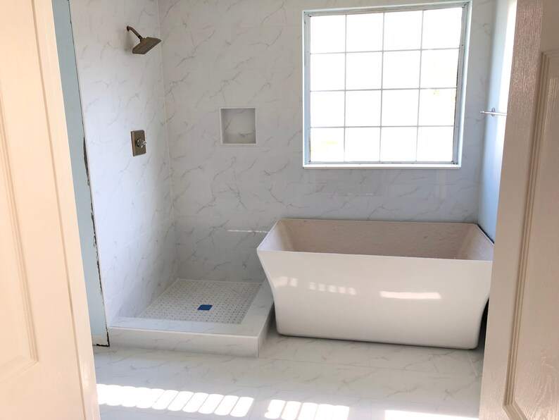 May include: A white bathtub with a white tiled floor and a shower stall with a white tiled floor and a white tiled wall. The shower stall has a shower head and a shower handle.