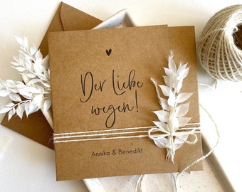 Peut inclure: Une carte marron avec le texte "Der liebe wegen!" et "Annika & Benedikt" écrit dessus. La carte est décorée de fleurs séchées blanches et de ficelle.