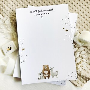 Könnte beinhalten: Weißes Schreibwarenset mit einer Illustration von Bär, Lama und Fuchs. Der Text "sei wild, frech und einfach WUNDERBAR" ist oben aufgedruckt. Enthält einen kleinen, quadratischen Behälter mit einem Bienenmuster.