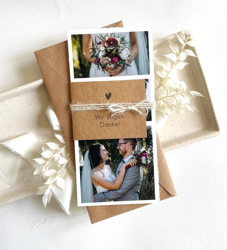 May include: A brown card with a white border and two photos. The top photo shows a bouquet of flowers. The bottom photo shows a couple embracing. The card has a small heart and the text "Wir sagen Danke!" in brown.