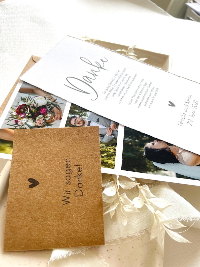 May include: A thank you card with a simple design and a handwritten message in German. The card is decorated with a small heart and a photo of a bouquet of flowers. The text on the card reads "Danke" and "Wir sagen Danke!"