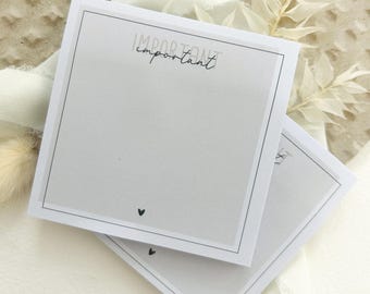 May include: Two white square notepads with a black border and the word "important" in cursive script. Each notepad has a small black heart at the bottom. The notepads are stacked on top of each other.