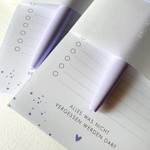 May include: Two white notepads with purple dots and a purple pen. The notepad has the text "ALLES WAS NICHT VERGESSEN WERDEN DARF" and a small purple heart.