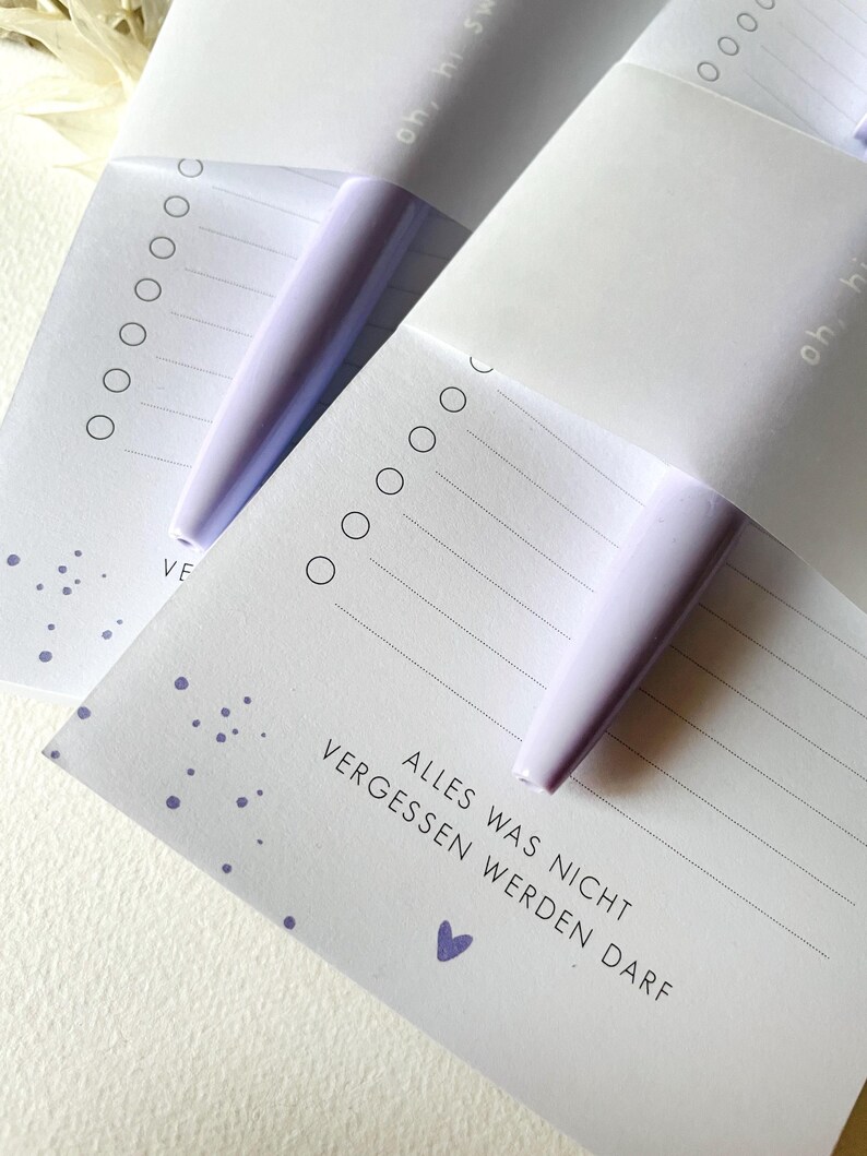 May include: Two white notepads with purple dots and a purple pen. The notepad has the text "ALLES WAS NICHT VERGESSEN WERDEN DARF" and a small purple heart.
