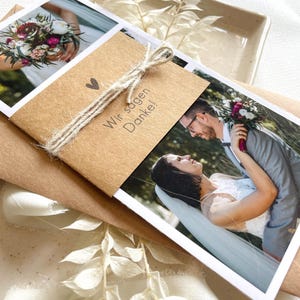May include: A brown card with the text "Wir sagen Danke!" tied with twine and a heart symbol. The card is decorated with two photos, one of a bouquet of flowers and another of a couple embracing.