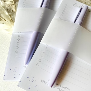 May include: Two white shopping list pads with purple pens. The pads have a dotted pattern and the text "Einkauf" and "oh, hi sweetie" on them. The text "WAS NICHT" and "VERGEN WERDEN DARF" is on the bottom of the pad.