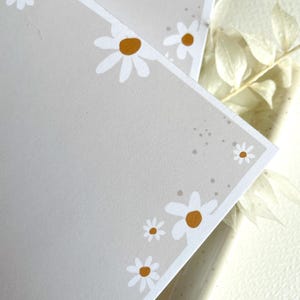 May include: Two gray cards with a white border and white daisies with yellow centers. The daisies are arranged around the edges of the cards.