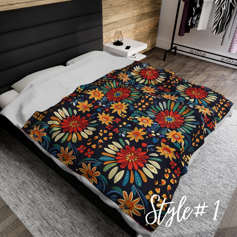 May include: A black and white floral patterned throw blanket with red, yellow, blue, and green flowers. The blanket is folded and displayed on a bed.