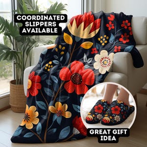 May include: A dark blue throw blanket with a floral pattern featuring red, yellow, and white flowers. The blanket is draped over a chair and there are matching slippers in the foreground. The text "COORDINATED SLIPPERS AVAILABLE" and "GREAT GIFT IDEA" are also visible.