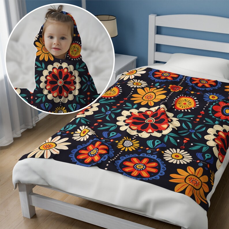 May include: A black and white floral patterned throw blanket with red, yellow, and blue accents. The blanket is folded on a white bed frame with a white headboard.