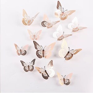 May include: A set of 12 decorative 3D butterfly wall decals in gold, white, and pink. The butterflies have a delicate, cut-out design and are perfect for adding a touch of whimsy to any room.