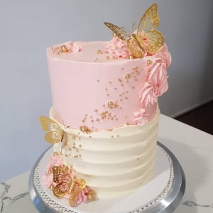 May include: Two-tiered pink and white cake decorated with gold butterflies, gold beads, and pink frosting flowers.
