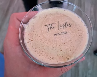 May include: A clear glass with a brown liquid inside. The glass has the text "The Lisles" and "10.02.2024" etched on the bottom.