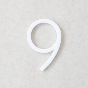 May include: White plastic number nine. The number is three-dimensional and has a rounded shape.