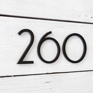 May include: Black metal house numbers, 260, mounted on a white wooden surface.