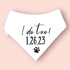 May include: White dog bandana with the text "I do too!" in black script, along with the date "1.26.23" and a paw print. The bandana is triangular and has a small tag on the side.