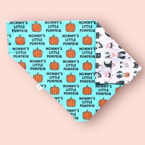 May include: A triangular pet bandana featuring a bright turquoise background with a repeating pattern of orange pumpkins and the black text "MOMMY'S LITTLE PUMPKIN". The reverse side displays a white fabric with a pattern of various dog faces.