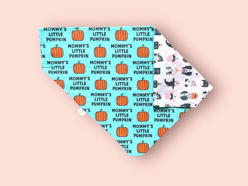 May include: A triangular pet bandana featuring a bright turquoise background with a repeating pattern of orange pumpkins and the black text "MOMMY'S LITTLE PUMPKIN". The reverse side displays a white fabric with a pattern of various dog faces.