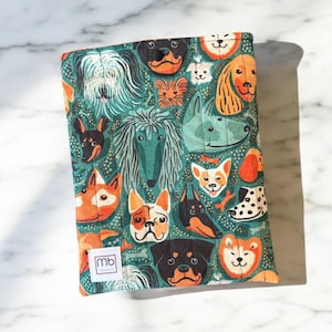 May include: A rectangular quilted fabric sleeve featuring a repeating pattern of various dog breeds on a dark teal background. The sleeve includes a small white rectangular label with the black text mb printed on the bottom left corner.
