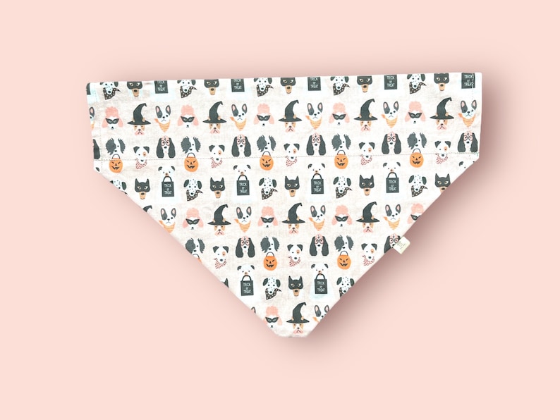 May include: A triangular pet bandana featuring a repeating pattern of various dog breeds dressed in Halloween costumes, including witch hats, masks, and glasses, alongside orange jack-o'-lanterns and black trick-or-treat bags on a white background.