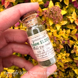 May include: A small glass bottle with a cork stopper filled with green powder. The label reads "RUGGANS.COM Ogham ELDER Whole Tree Powder Ruis - R - Vine prepared whole Elder tree powder of the energies, all of the potential."