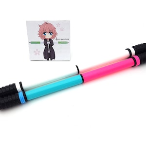 May include: Two double-ended pens with black, white, and colored barrels. The pens are on a white surface. The pen on the top is white with a pink barrel. The pen on the bottom is turquoise with a pink barrel.