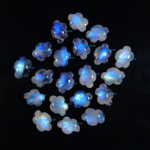 May include: A collection of 18 white moonstone cabochons, each carved in a cloud shape with a blue iridescent sheen. The stones are scattered on a black background.