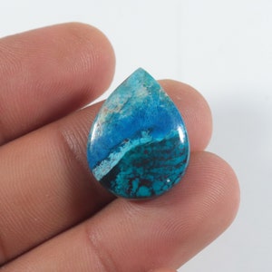 May include: A teardrop-shaped cabochon gemstone with a blue and green colour pattern. The stone has a mottled appearance with shades of turquoise, blue, and green.